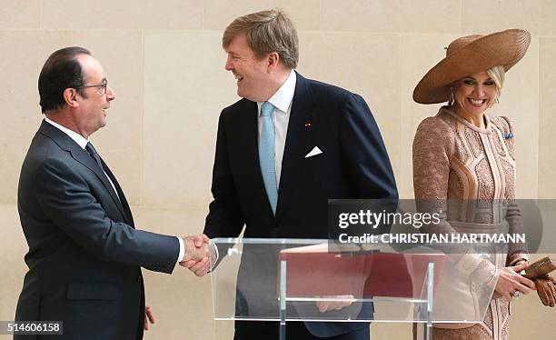 French President Francois Hollande shakes hands with King Willem Alexander of the Netherlands as Queen Maxima looks on after signing the visitor's...