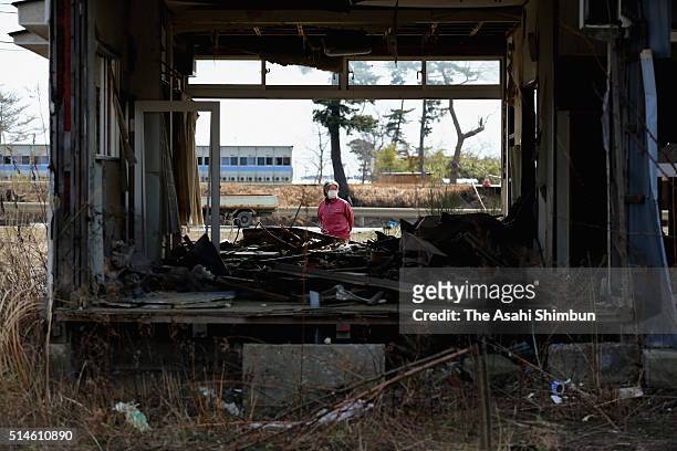 Woman walks past a destroyed house which remains without being demolished a day before the fifth anniversary of the Great East Japan Earthquake and...