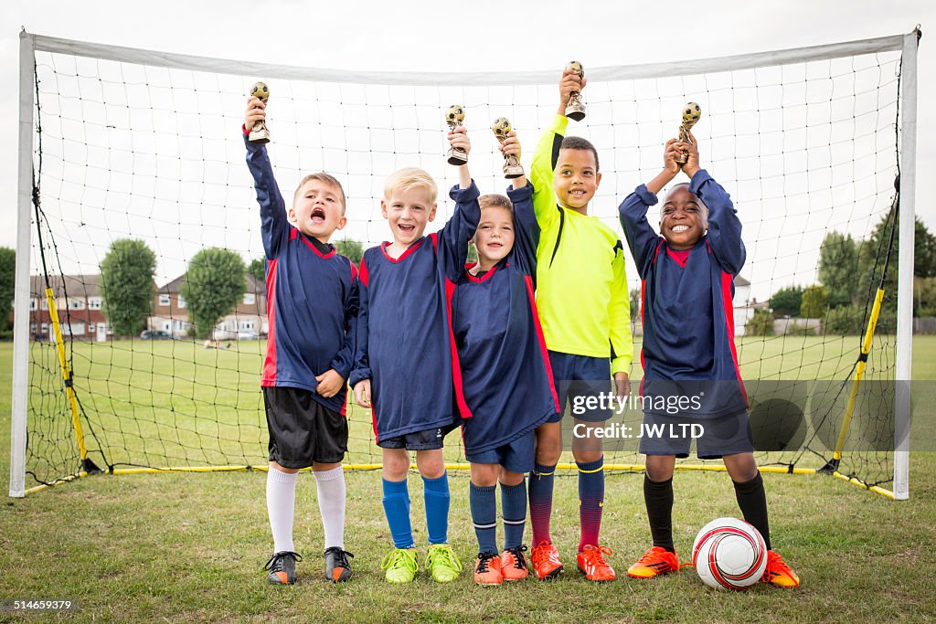 Five boys standing in football goal with trophies