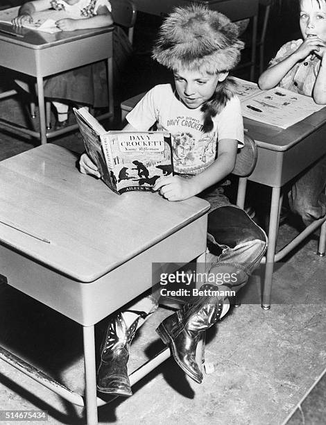 Young boy reads about American pioneer legend Davy Crockett while wearing a Coon-skin cap and a Davy Crockett t-shirt.
