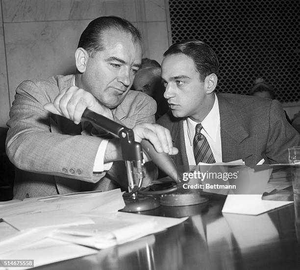 Senator Joseph McCarthy covers a microphone while Roy Cohn talks to him during a televised subcommittee meeting