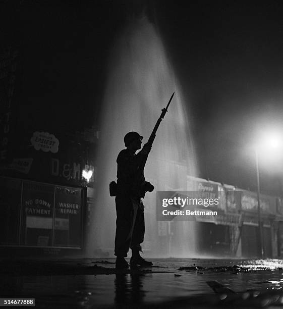 Los Angeles, CA: Silhouetted by the cool gush of a broken fire hydrant, a National Guardsman stands ready for further trouble in the strife-torn...