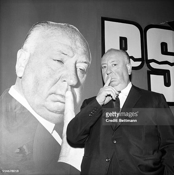 Alfred Hitchcock poses next to a picture of himself on a poster for his film Psycho while in Paris.