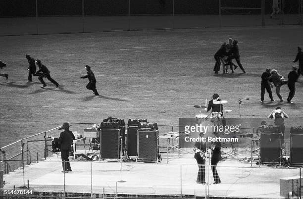 Policemen clear the field of enthusiastic fans as The Beatles perform on a bandstand in Candlestick Park, San Francisco, California.