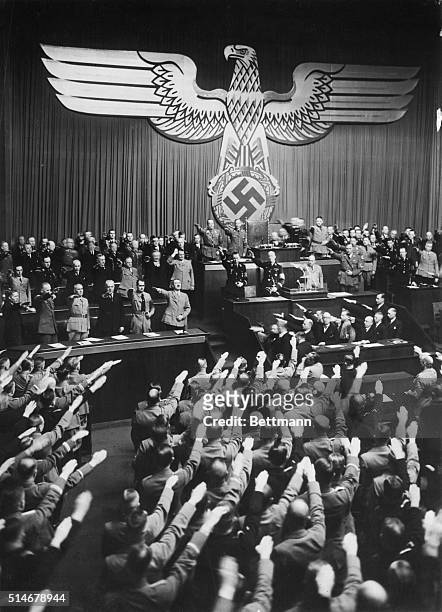 The members of the Reichstag salute during the playing of the German national anthem, after Hitler had denounced the war guilt clause contained in...
