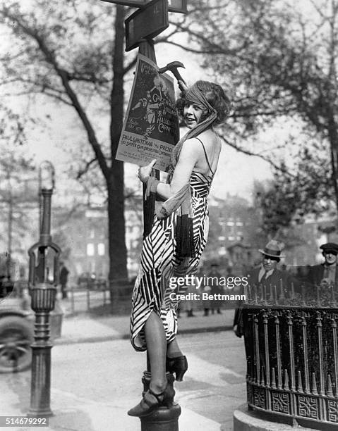 Flapper hangs a poster to advertise the Greenwich Village Halloween Ball, at which Paul Whiteman is to perform.
