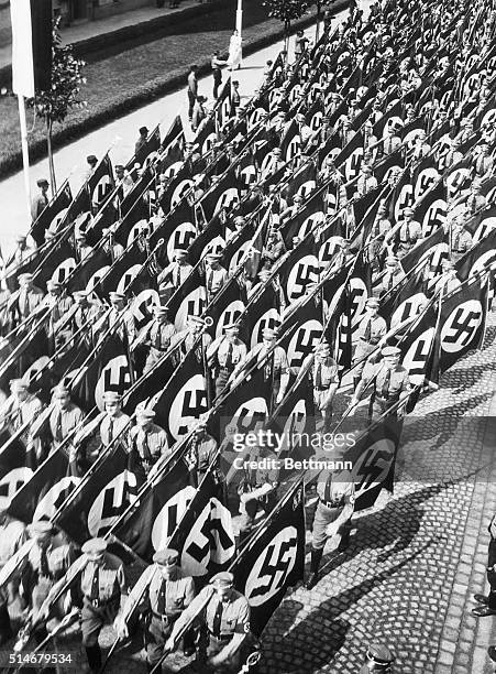Nazis march through the streets of Nunberg to the Nazi Part Congress carrying flags adorned with swastikas which have just be adopted as the sole...