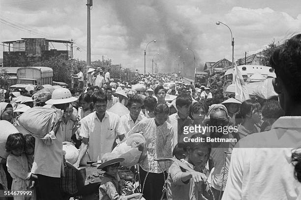Saigon:While the battle blazes on behind them, refugees from Saigon's Chinese Cholon section stream across a bridge where they are loaded into trucks...