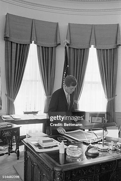Washington, DC: President John F. Kennedy lives on his feet, standing more during the day than sitting. Here Kennedy examines a picture presented to...