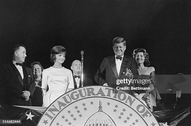 President-elect John F. Kennedy stands with wife Jackie and smiles at the applause given to him at the pre-Inaugural gala. Also on the podium is...