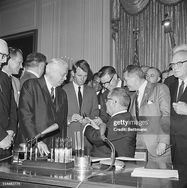 President Lyndon Johnson hands several fountain pens to Attorney General Robert Kennedy during the signing ceremony of th Civil Rights Act. The bill...