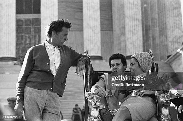 Elizabeth Taylor sits in Eddie Fisher's lap on the set of Cleopatra while Richard Burton looks on. Taylor would soon leave Fisher for Burton.