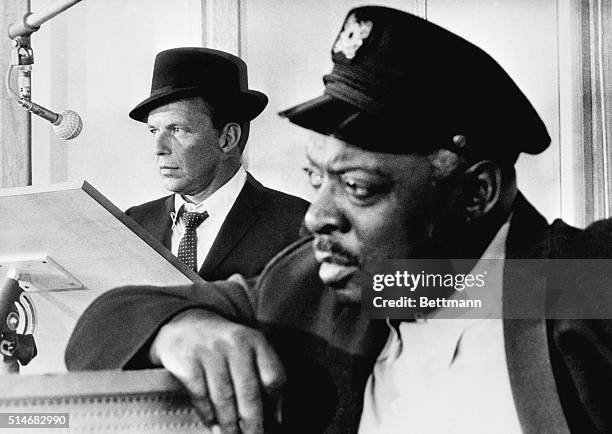 Count Basie leans in the foreground as Frank Sinatra stands at a lectern near a microphone. Sinatra worked on arrangements with Basie and toured with...