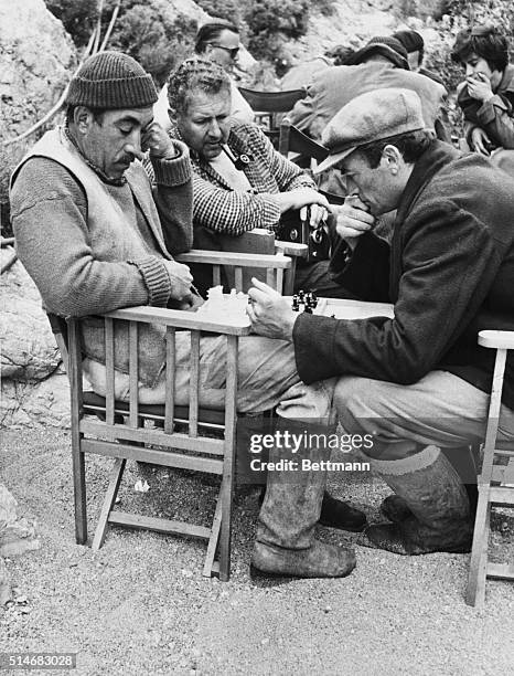 Gregory Peck and Anthony Quinn play chess between takes during the filming of The Guns of Navarone. Anthony Quayle looks on.