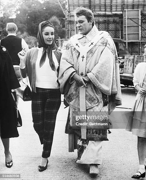 Elizabeth Taylor and Richard Burton stroll around the set where Burton is filming Becket. Burton is still in costume.