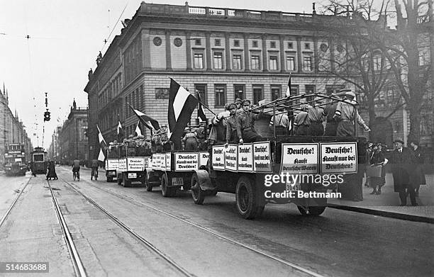 Caravan of trucks rolls through a street in Berlin, carrying Nazi stormtroopers on their way to boycott Jewish businesses, and bearing signs...