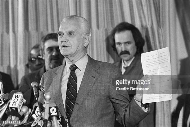 At a press conference, General William Westmoreland holds up a copy of a statement, signed by all principals, of the out-of-court settlement,...