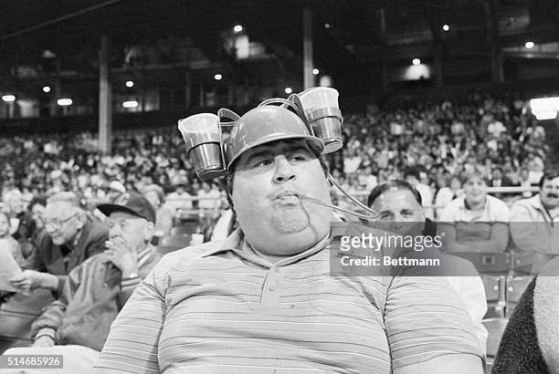 Baseball fan Neil P. Mullen sips from a tube leading to cups of beer attached to his baseball cap while enjoys a baseball game between the Cleveland...
