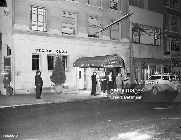 Taxi pulls up to the entrance of The Stork Club as people standing under the awning watch.