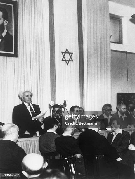 New Prime Minister David Ben-Gurion reads the proclamation declaring the existence of the New Jewish State. Attending the announcement are delegates...