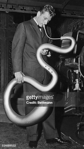 Hollywood, CA: Top comedy man Danny Kaye, playing a Renaissance-type serpent instrument in one of his ad-lib, off-stage routines between takes of...