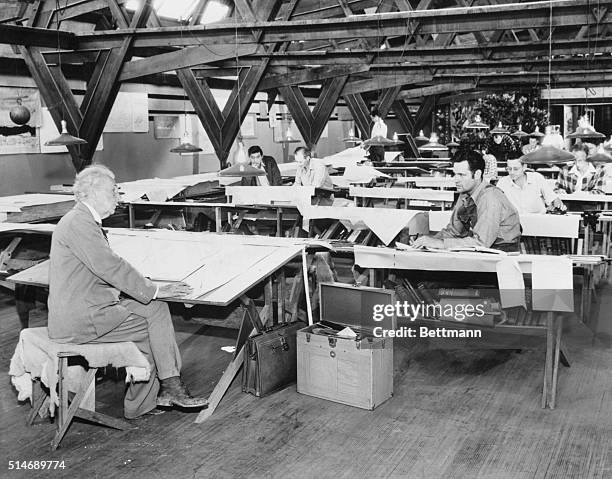 Architect Frank Lloyd Wright discusses plans with William Wesley Peters while other apprentices work at their drafting tables.