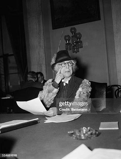 Washington, DC: Jeanette Rankin, before Senate Naval Affairs Committee. Miss Rankin is wearing a jaunty hat with a feather and is pointing at her eye.