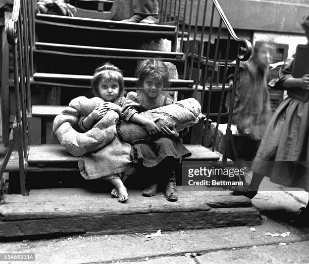 Two small girls in a New York slum sit on a stairway and clutch a giant bread loaf and pretzel, 1890.