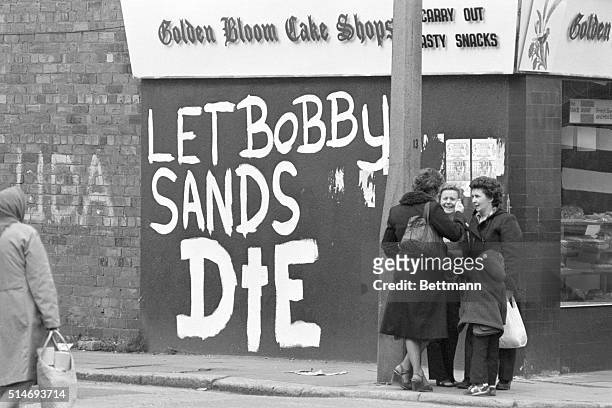 Three women talk casually near a graffitied message directed toward hunger striker Bobby Sands well in to his protest against British forces in...