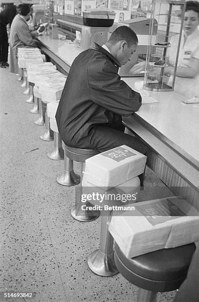 An African-American student sits at a lunch counter reserved for white customers during a sit-in to protest segregation. Packages of napkins have...