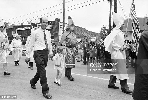 Young girl, holding hands with robed Ku Klux Klansmen, walks in a parade to support the Vietnam War. An African American protester at the parades...