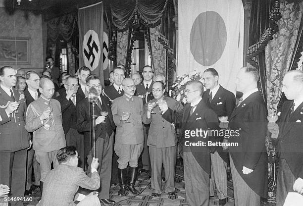 Against a background of their respective flags, German and Japanese officials toast the new Axis Pact in Tokyo. At extreme right is Heinrich Stahmer,...