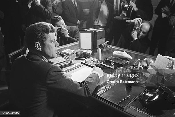 Reporters take pictures of President Kennedy behind his desk, after signing the arms embargo against Cuba. The embargo effectively quarantined Cuba.