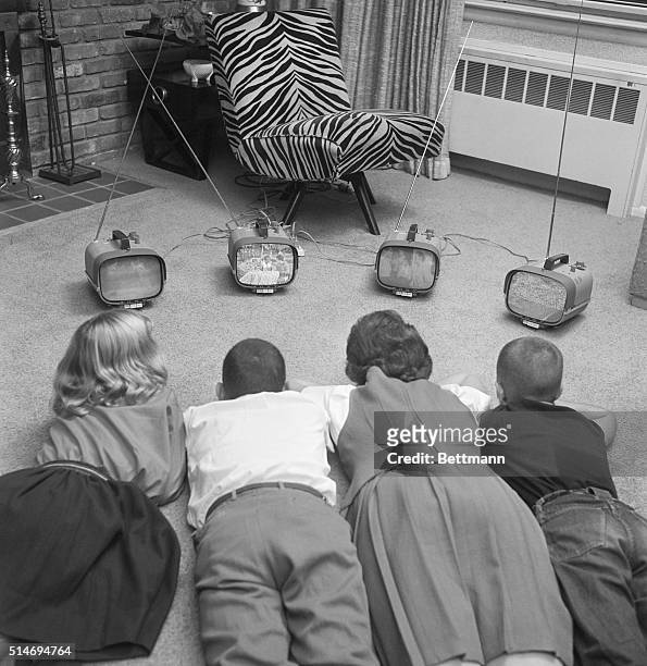 Four children watch four different small televisions on a living room floor.