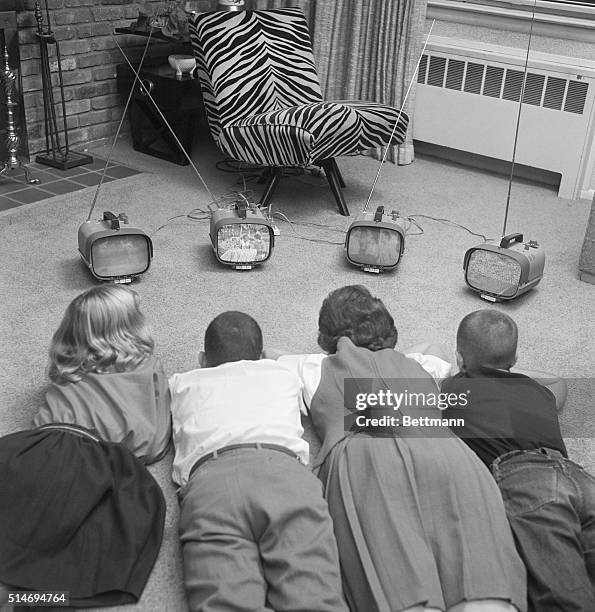 Four children watch four different small televisions on a living room floor.