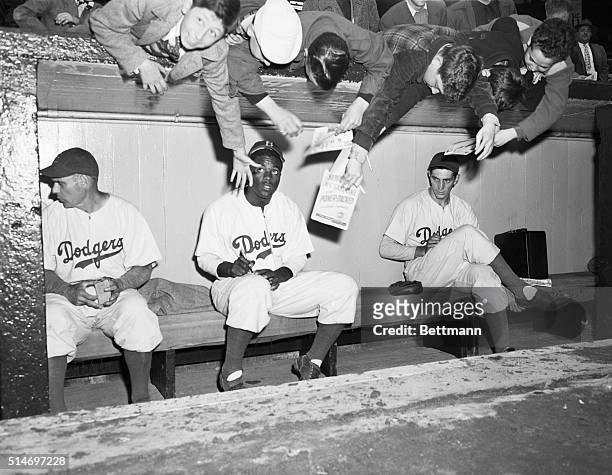 New York, NY: Youthful Brooklyn Dodger's rooters and fans, reach over from behind the dugout at Ebbets field today, trying to get an autograph from...