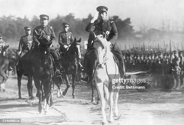 Emperor Hirohito salutes as he rides past and inspects his troops.