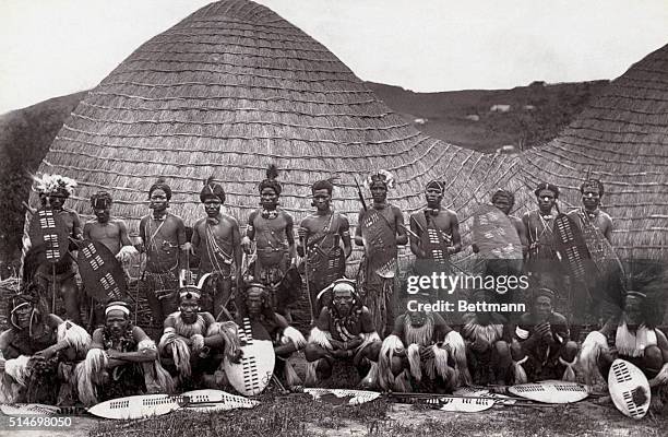 Group of Zulu warriors wear traditional dress and carry shields.