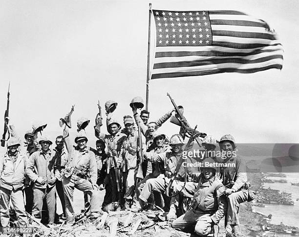 United States Marines pose on top of Mount Suribachi on the island of Iwo Jima with the American flag.