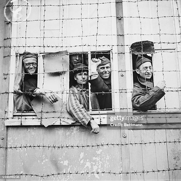 Dachau Internment Camp: Prisoners look out from barbed wire fence around camp. Filed 5/12/45