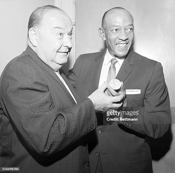 Olympic medalist Jesse Owens hands one of his gold medals to Sam Greller to place in the Hall of Fame of Jamaica in 1962.