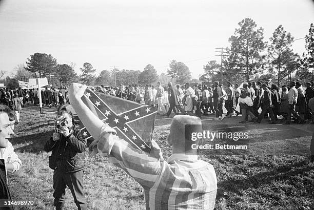 Marchers participating in the Selma to Montgomery civil rights march walk past a white youth holding a confederate flag.