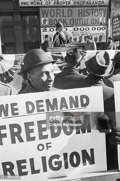 Black Muslim carries a sign reading "We Demand Freedom Of Religion," while Malcolm X speaks behind him at a rally in Harlem. Malcolm X was protesting...