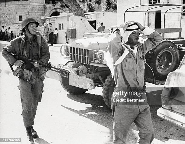 An Israeli soldier marches a soldier from Jordan through the streets of Bethlehem. The captive was found without identification papers after Israeli...