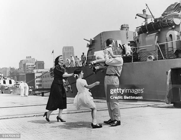 Navy officer greets his wife and two daughters on the dock next to a Navy ship, after returning from duty in the Pacific. California. Circa 1940s.