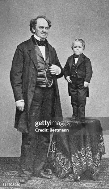 Barnum, circus producer, stands next to a table on which Charles Stratton, a dwarf who came to be known as Tom Thumb, stands. Barnum hired Stratton...