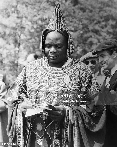 Epsom, England: A colorful racing fan at Epsom Downs is the Fon of Bali, from the British Cameroons. Dressed in elaborate national costume, he looks...