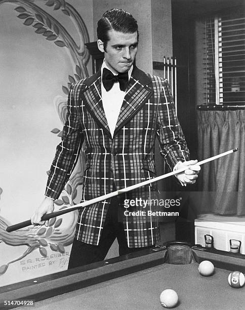 Man models the latest "dressed up casual" look of a plaid jacket and bow tie for playing pool in the early 1970s.