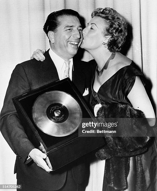 London, England: Record sets a kiss. Smiling bandleader Mantovani bemas as he receives a kiss from singer Vera Lynn on top of his other joys --...