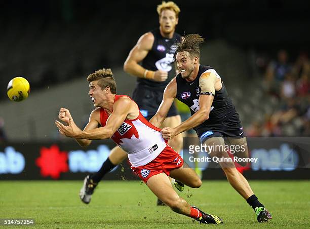 Jake Lloyd of the Swans handballs whilst being tackled by Dale Thomas of the Blues during the NAB Challenge AFL match between the Carlton Blues and...